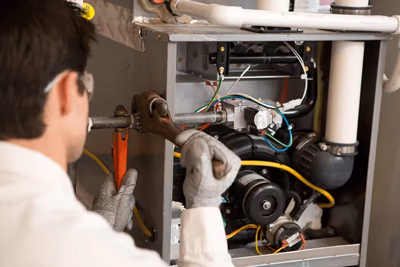 Technician using pipe wrenches on furnace.