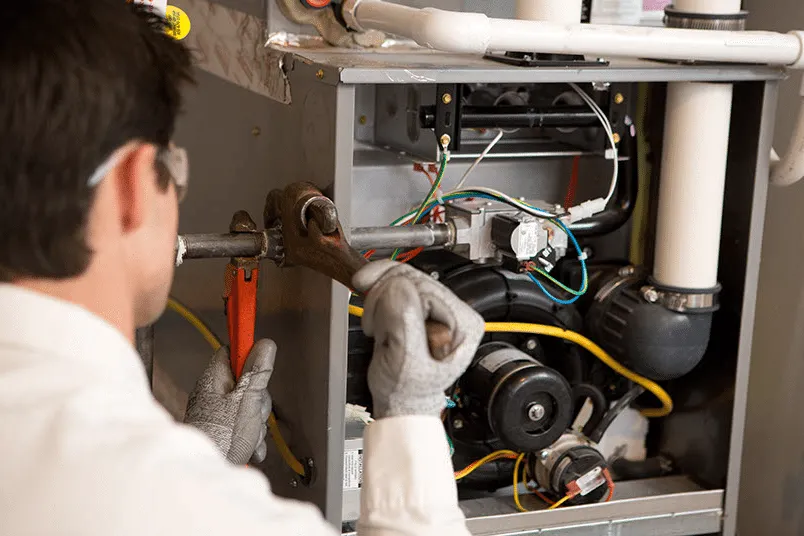 Technician using pipe wrenches on furnace.
