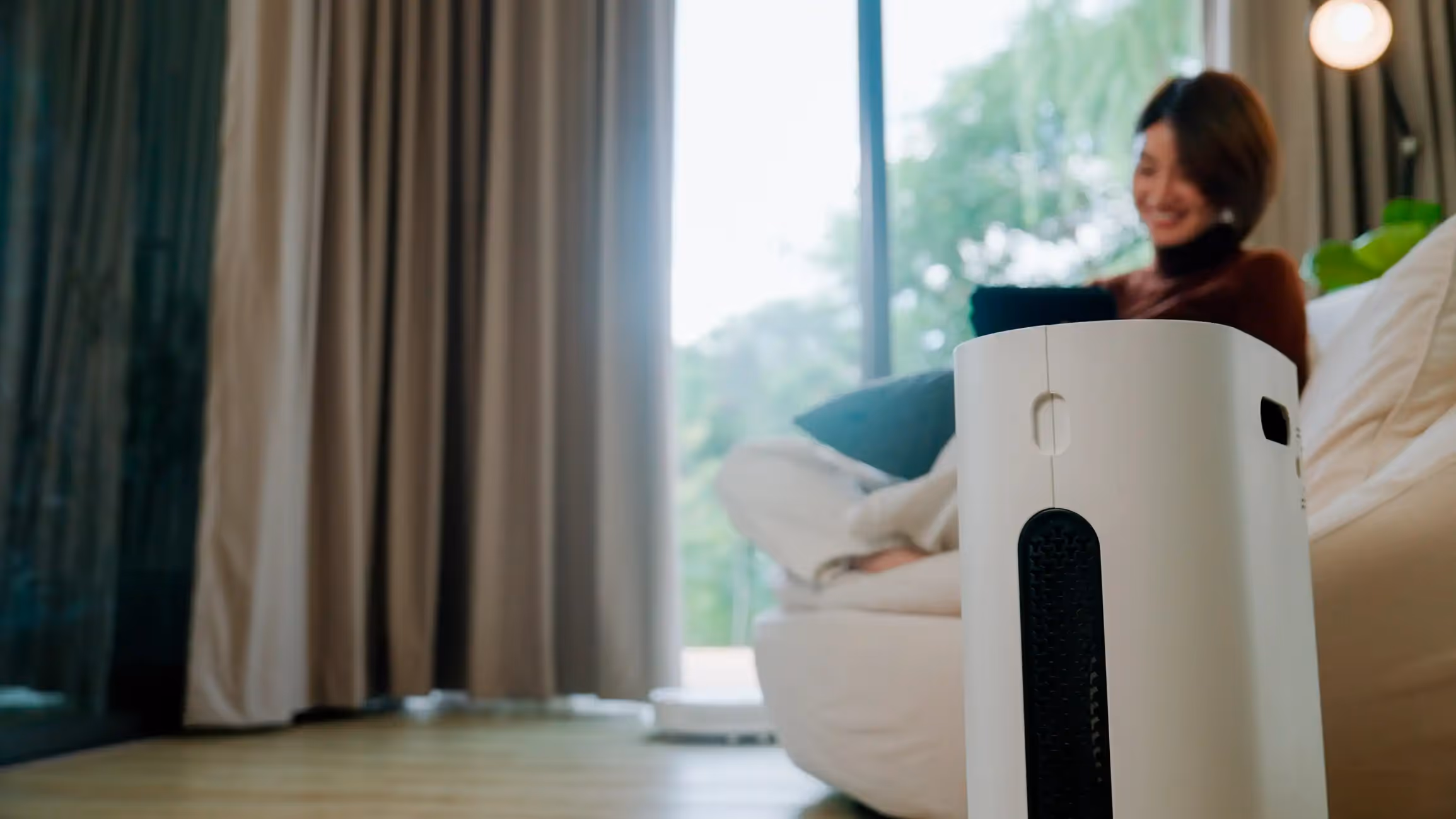 Air purifier near a woman relaxing on a sofa by a window.