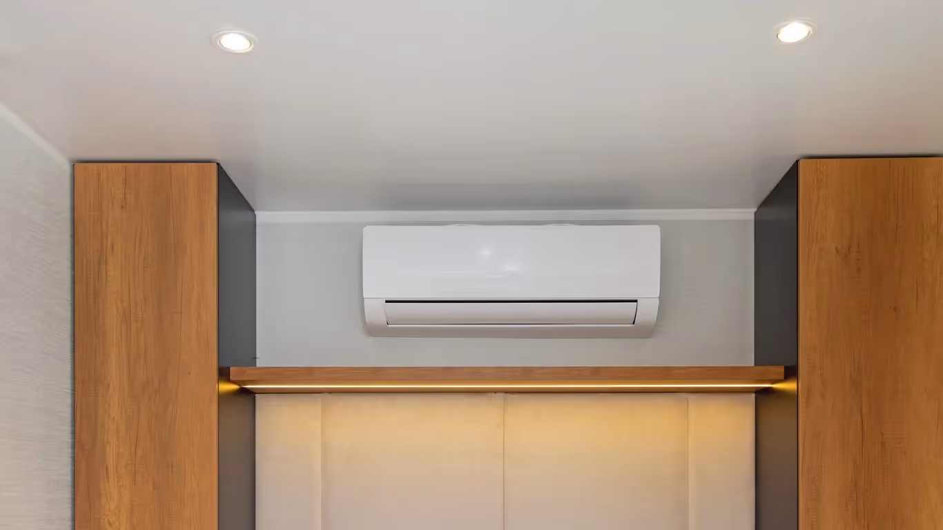 Wall-mounted white AC unit centered above recessed area with wood framing and built-in shelf lighting.
