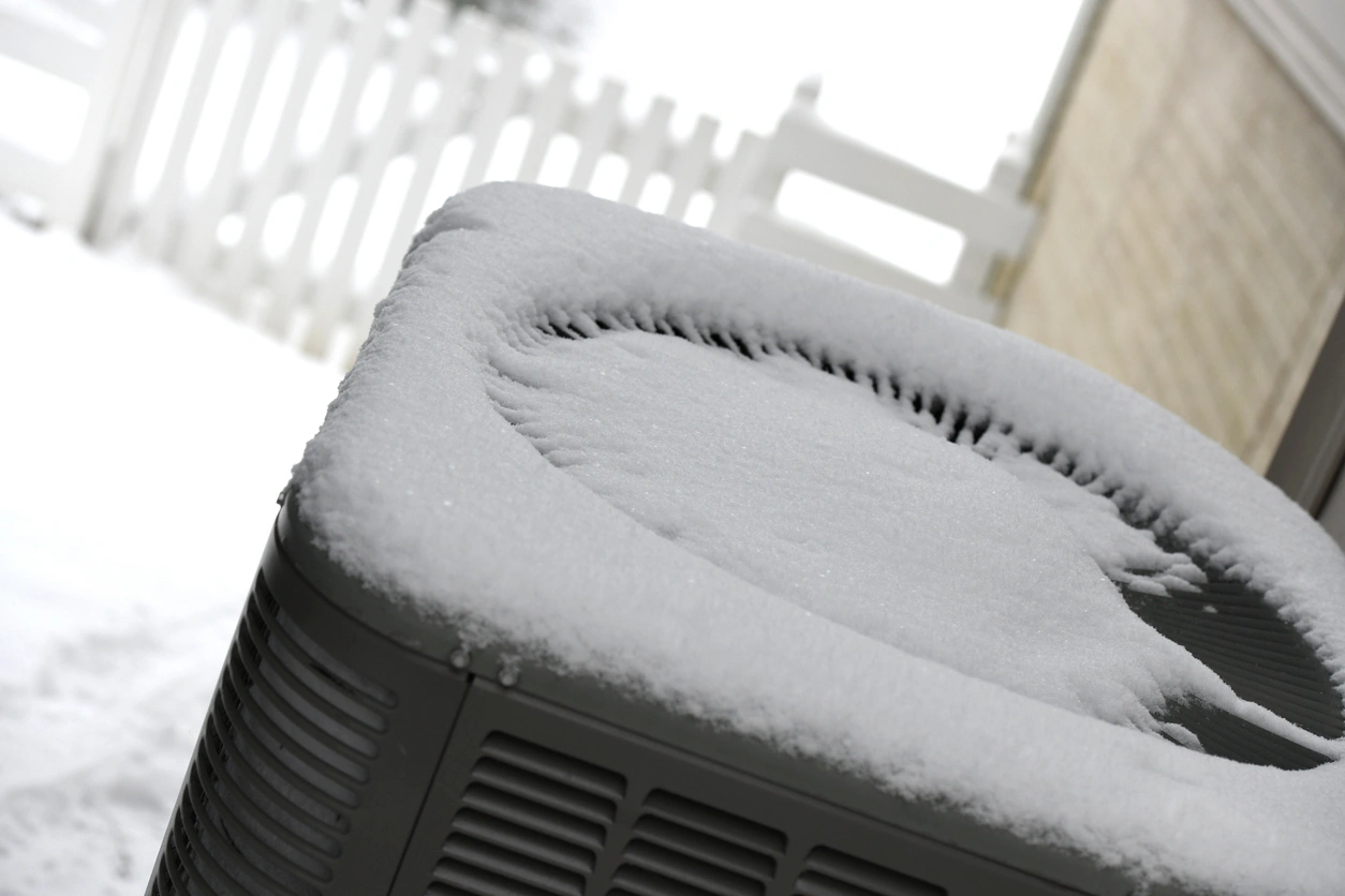 Air conditioning unit covered in a layer of snow, set outdoors on a snowy day. 