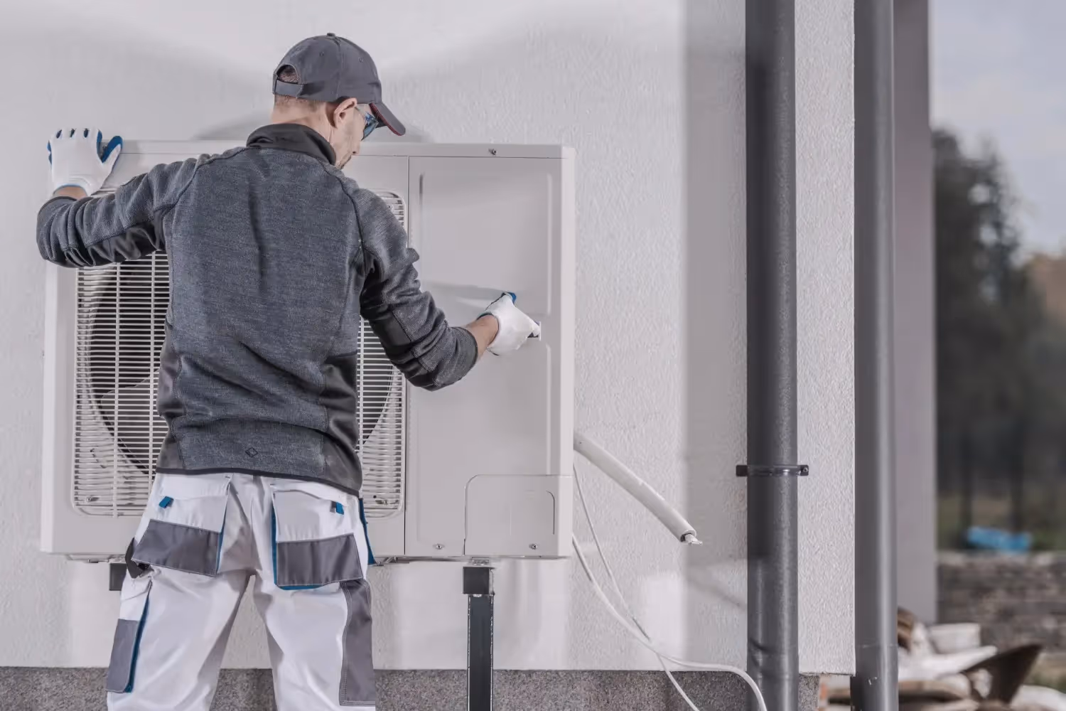 A technician in a gray and white uniform works on the casing of a wall-mounted mini-split unit