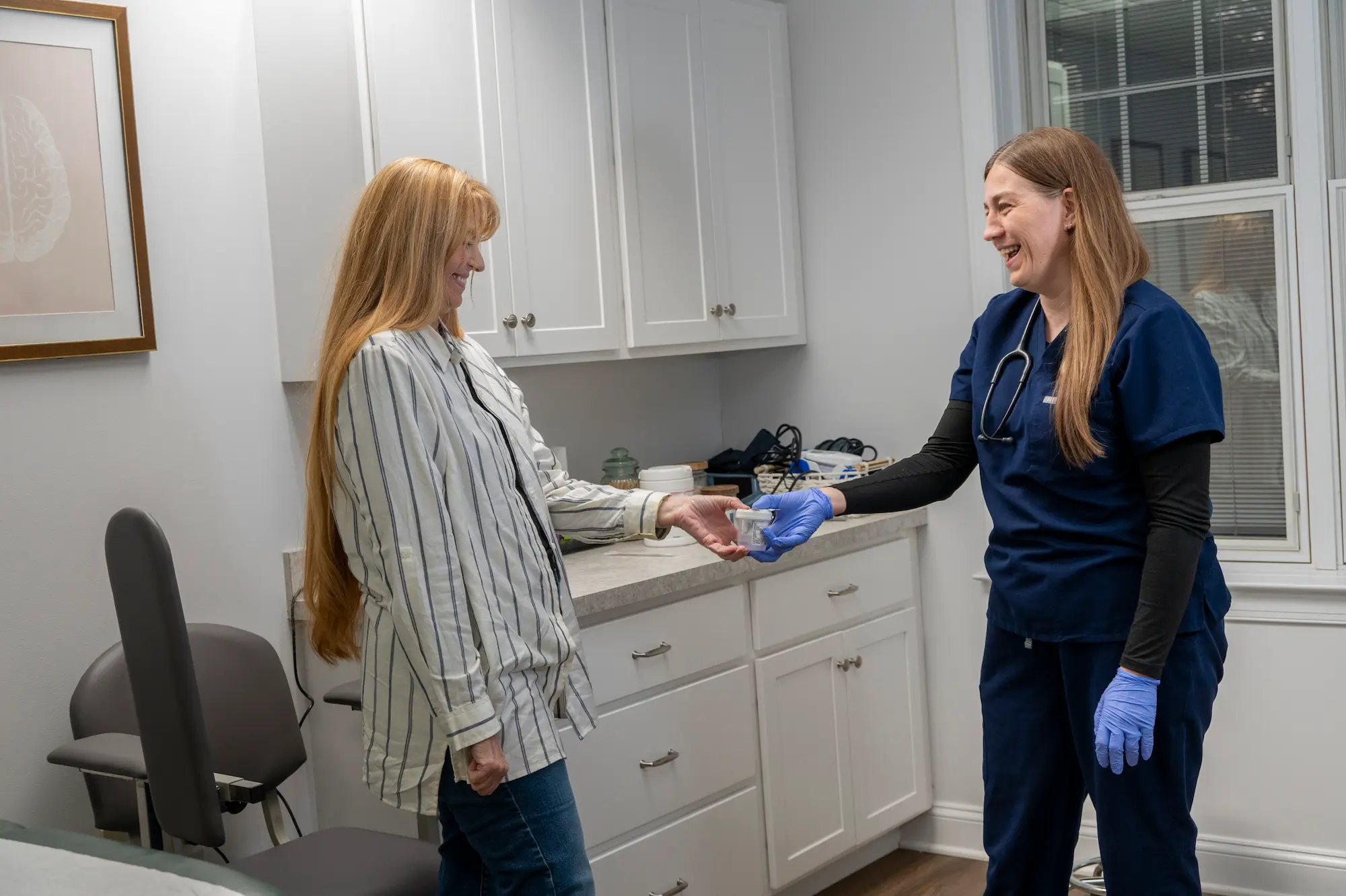 a healthcare provider laughing with a female patient while handing her a medical container