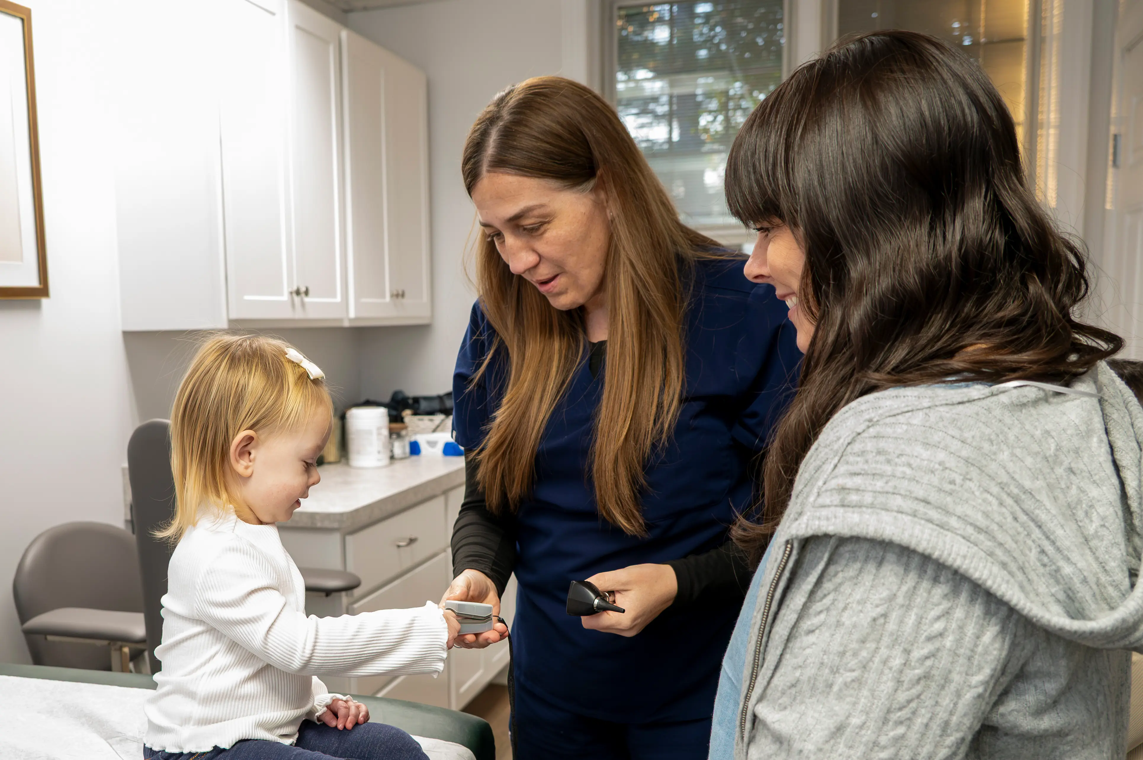 the provider giving a toddler girl a check up while her family looks on and smiles.