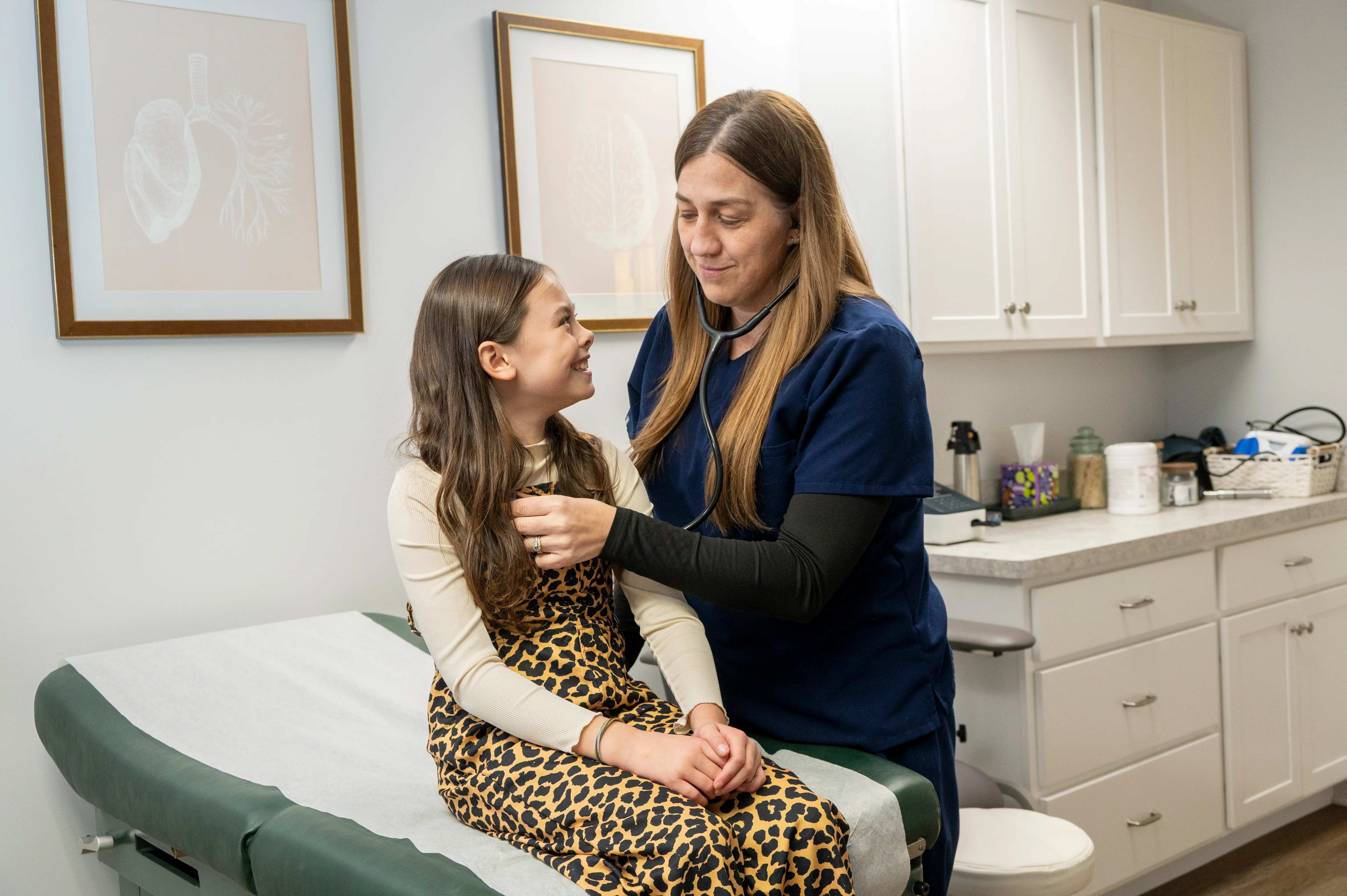 the healthcare provider listening to a child patient's heart while they smile at each other