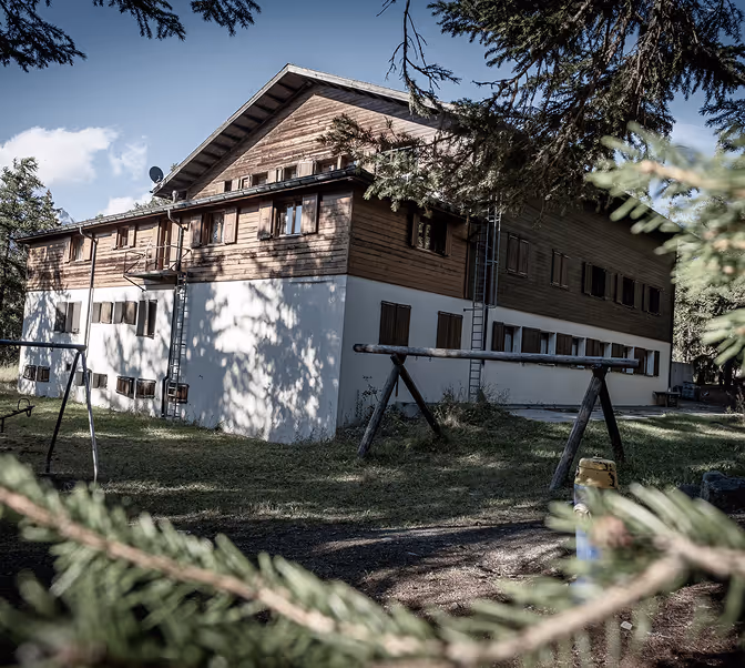 Das Bethania mit Holzwänden im oberen Bereich und weißem Putz im unteren Bereich, umgeben von Bäumen und mit einer Schaukel im Vorgarten.