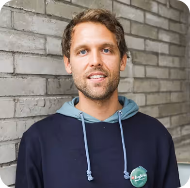 Portrait von Beat lächelnd vor einer grauen Backsteinwand.