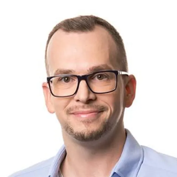 Muž s brýlemi a krátkými světlými vlasy, usmívající se do objektivu na bílém pozadí.