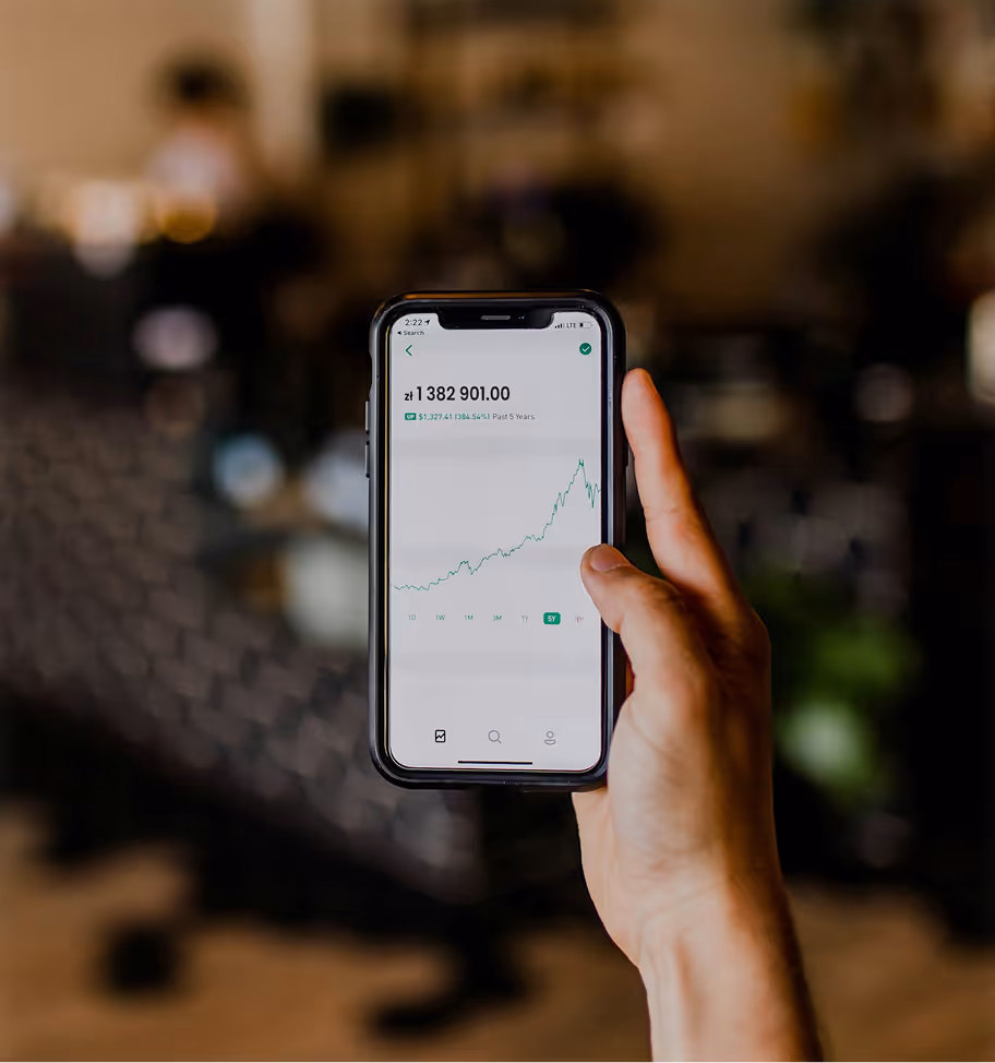 Ręka trzymająca smartfon wyświetlający pięcioletni wykres wzrostu rynku akcji o wartości 1 382 901,00 złotych polskich.