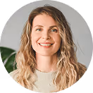 Lächelnde Frau mit lockigen, blonden Haaren vor grauem Hintergrund.