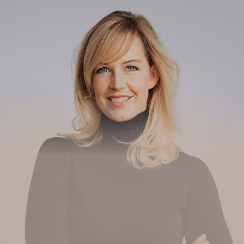 Lächelnde Frau mit blonden Haaren und schwarzem Rollkragenpullover vor grauem Hintergrund.