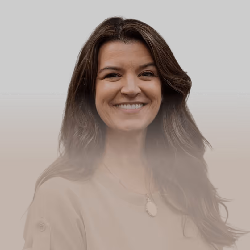 Lächelnde Frau mit langen braunen Haaren, trägt beiges Oberteil und Kette, dunkler Hintergrund.