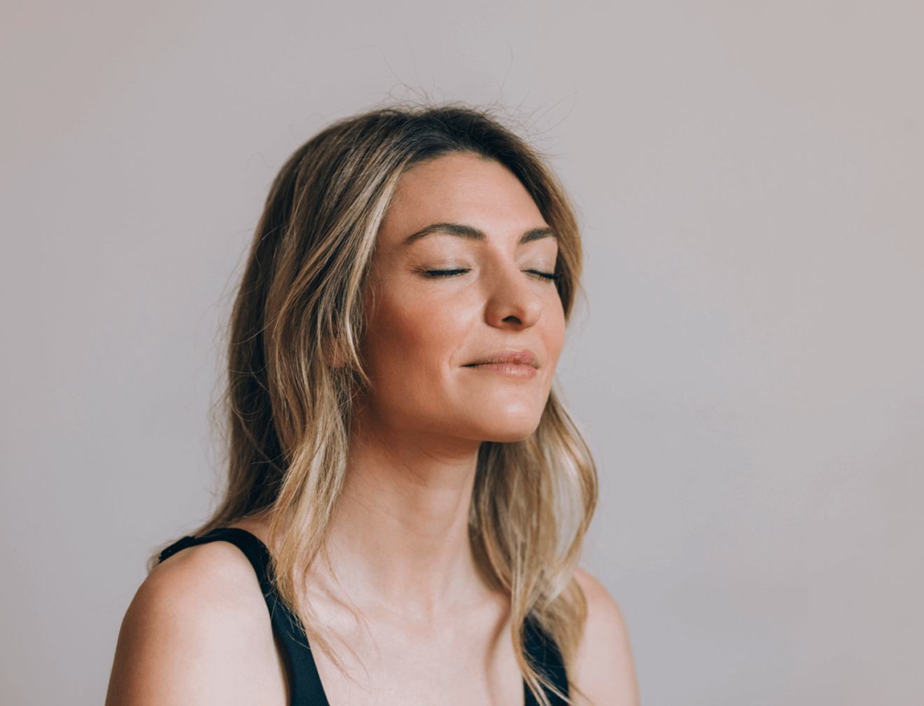 Frau mit geschlossen Augen und entspanntem Gesichtsausdruck, beigefarbener Hintergrund.