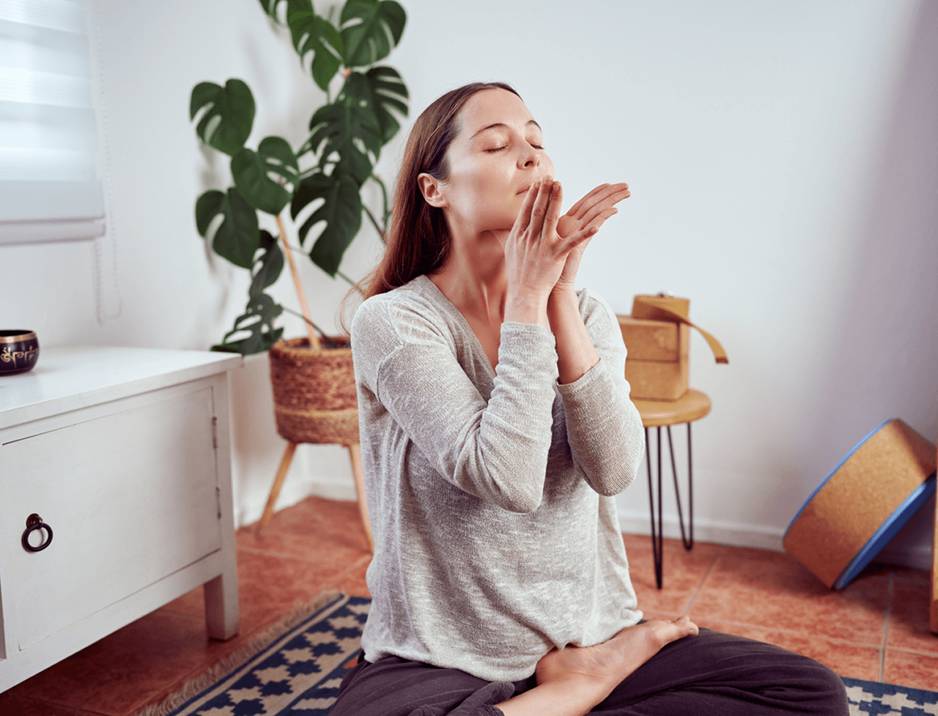 Frau praktiziert Yoga-Übung im Wohnzimmer, umgeben von Pflanzen und Meditationszubehör.