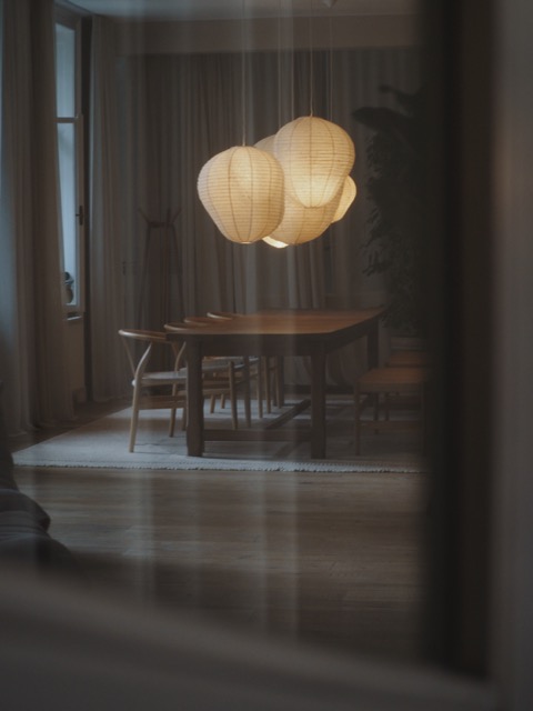 Cozy dining room with wooden table, chairs, and three glowing paper lanterns hanging above.