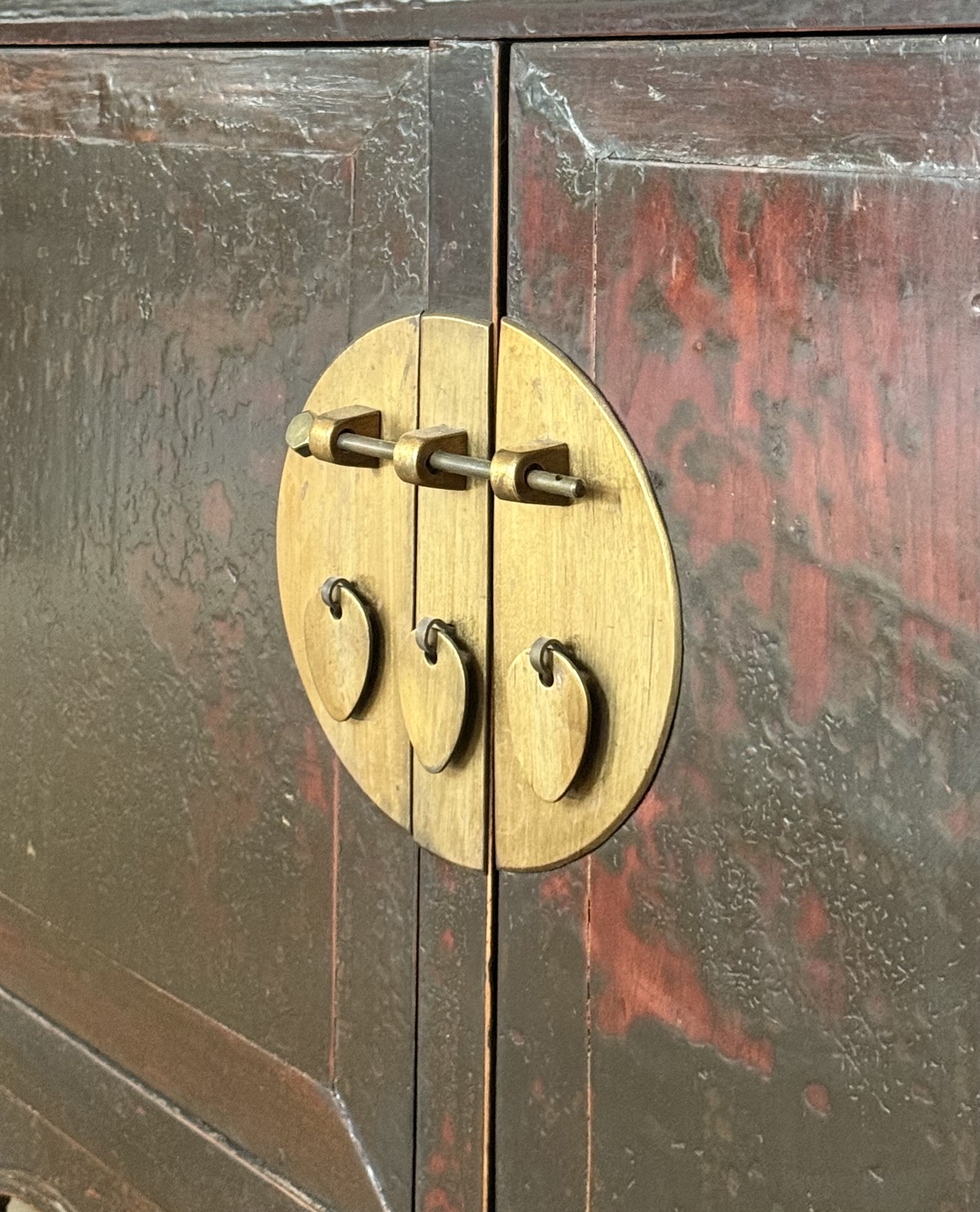 Close-up of an antique wooden cabinet door with a round brass latch and handles.