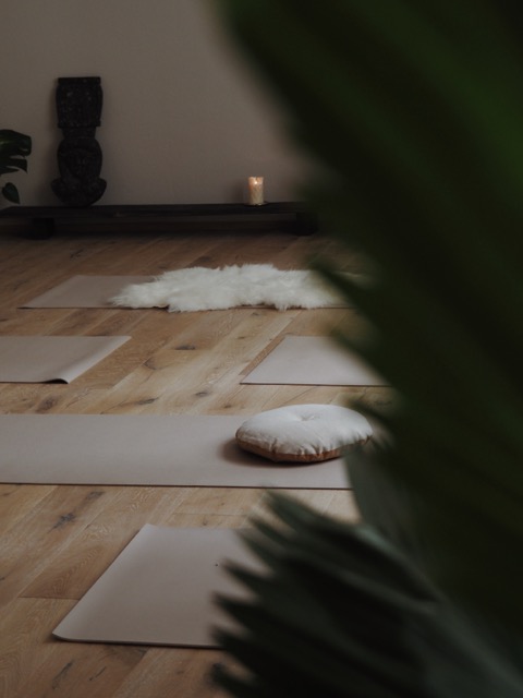 Yoga mats and meditation cushions arranged on a wooden floor in a calm, minimalist room.