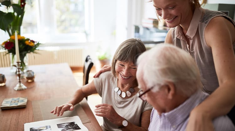A woman wraps her arms around her parents as they smile and look through a photo album together.