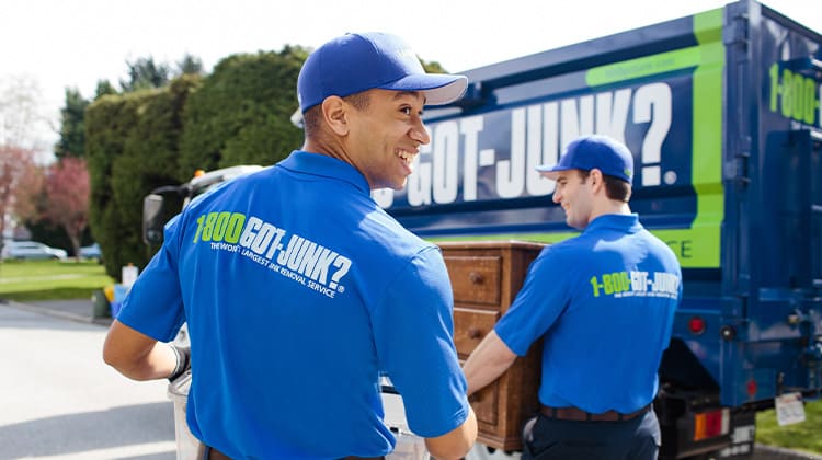 Two 1-800-GOT-JUNK? Truck Team Members smile while carrying away unwanted items.