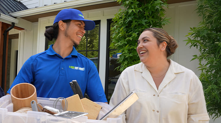 A woman and Truck Team Member, who is carrying a pile of junk, smiling at each other.