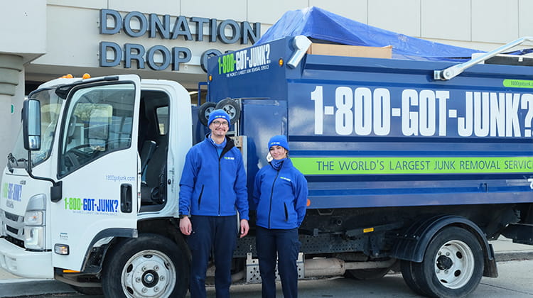 Two 1-800-GOT-JUNK? Truck Team Members standing in front of a branded junk removal truck parked near a donation drop-off area.