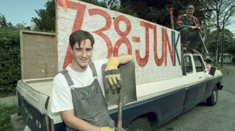 18 year old Brian Scudamore pictured in front of his first junk truck, with 738-JUNK written along the side of the truck in bold red lettering.