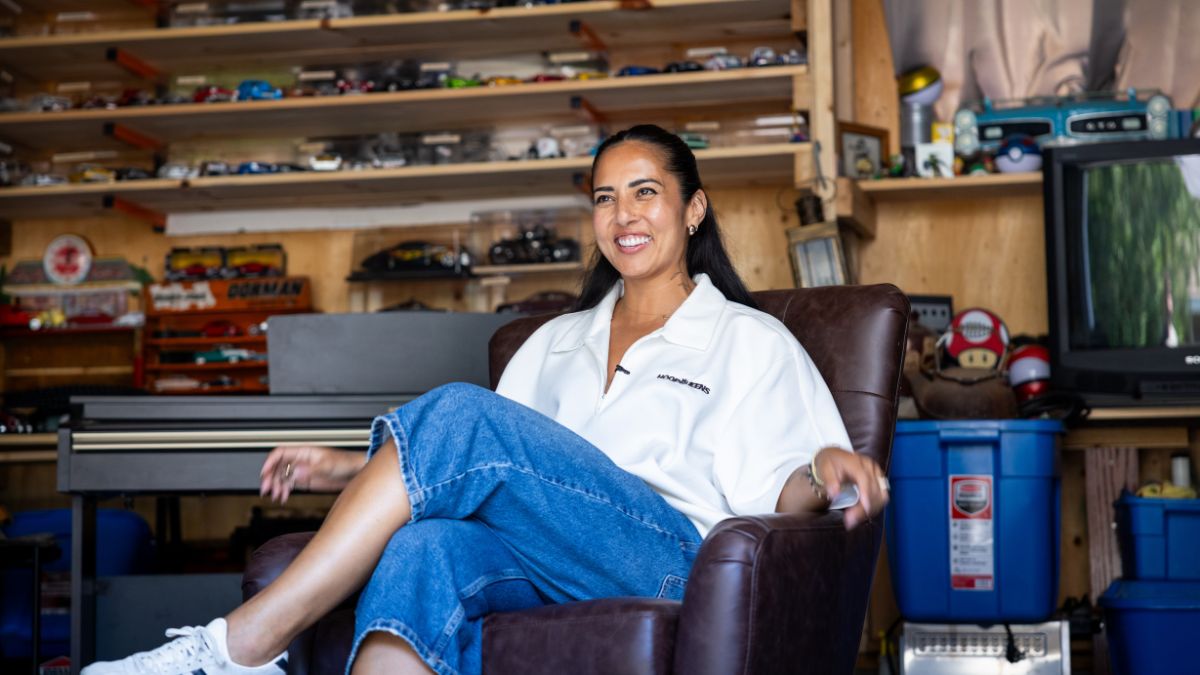 A smiling woman sitting in a leather armchair inside a garage filled with collectible toy cars, and household items before a 1-800-GOT-JUNK? cleanout.
