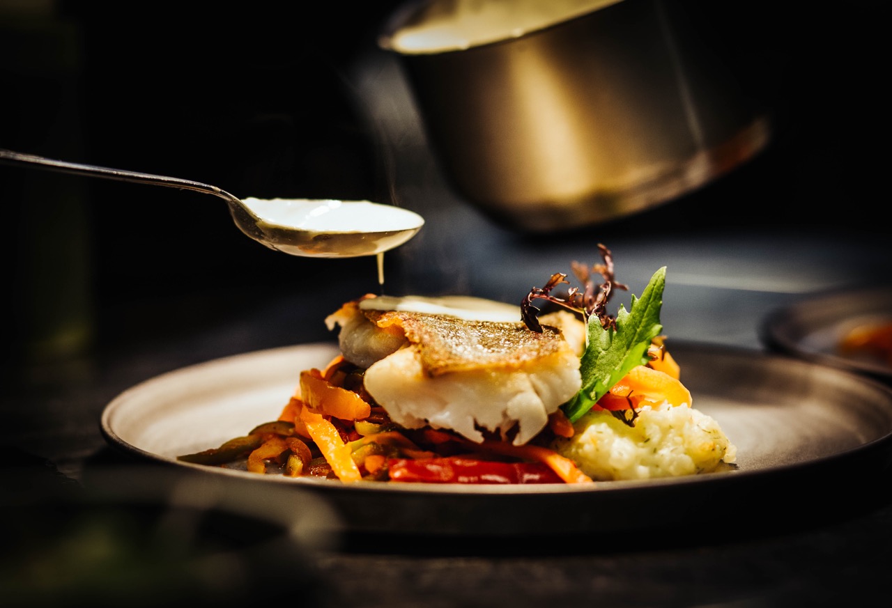 Sauce being poured on a fancy dinner plate with fish
