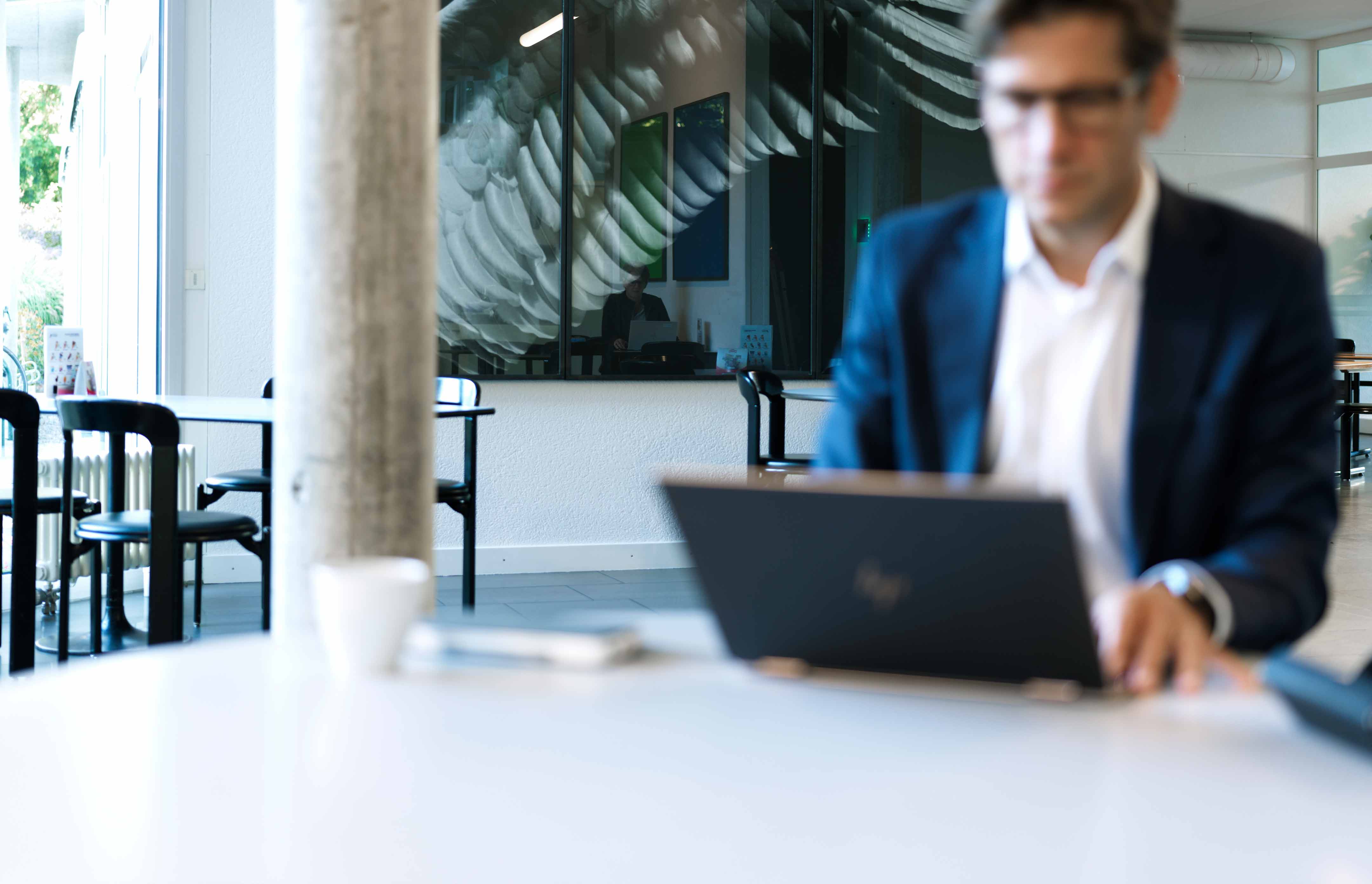 Ein Mann in einem blauen Anzug arbeitet mit einem Laptop an einem Tisch in einem hellen, modernen Café.