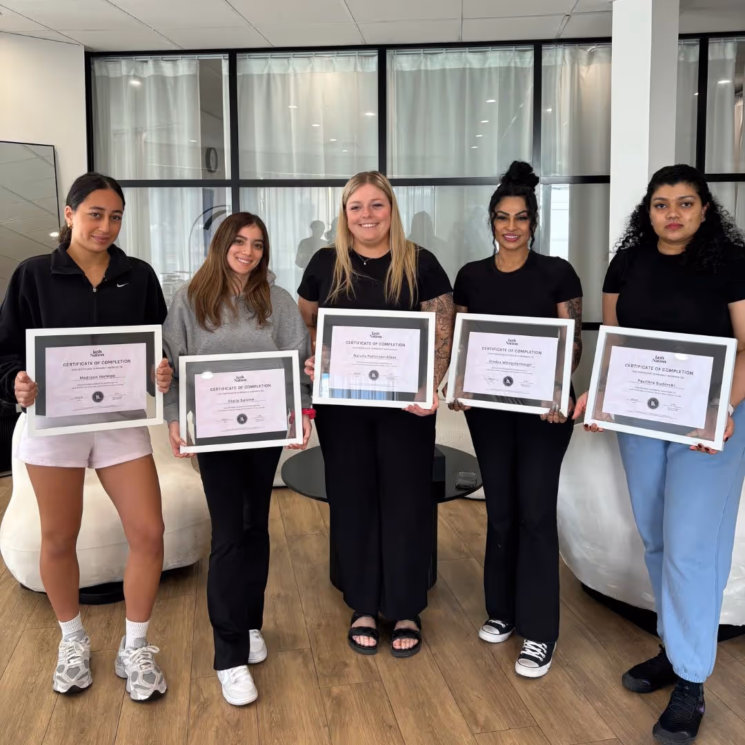 Five women standing indoors smiling and holding framed certificates of completion.