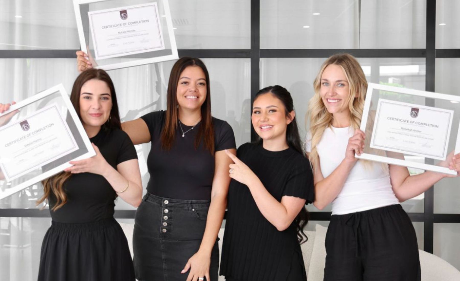 Four women standing and smiling, holding framed certificates of completion.