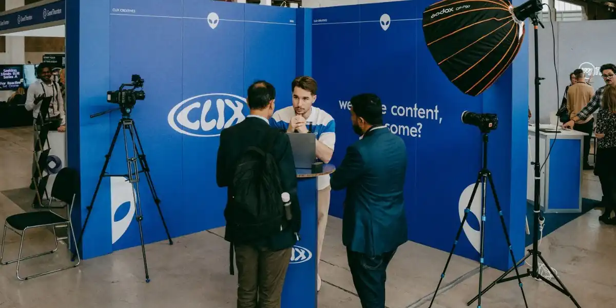 Video producer discussing a campaign brief with two clients at a CLIX Creatives stand, with cameras and lighting set up