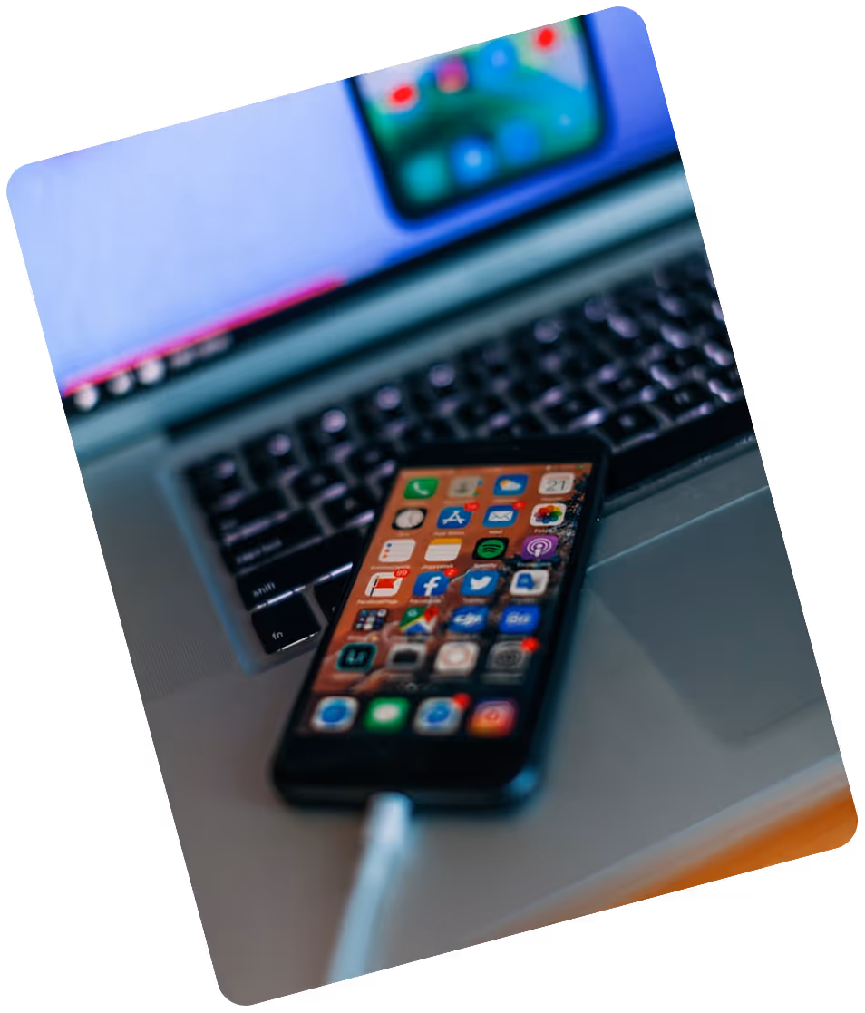 Smartphone with colorful app icons plugged in with a white charging cable, resting on a laptop keyboard.