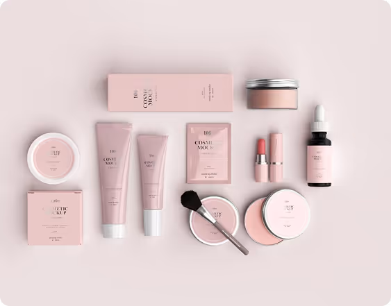 Flat lay of pink cosmetic products including tubes, jars, a dropper bottle, lipstick, and a makeup brush on a light pink background.