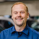 Smiling man with short light brown hair and a goatee wearing a blue collared shirt.