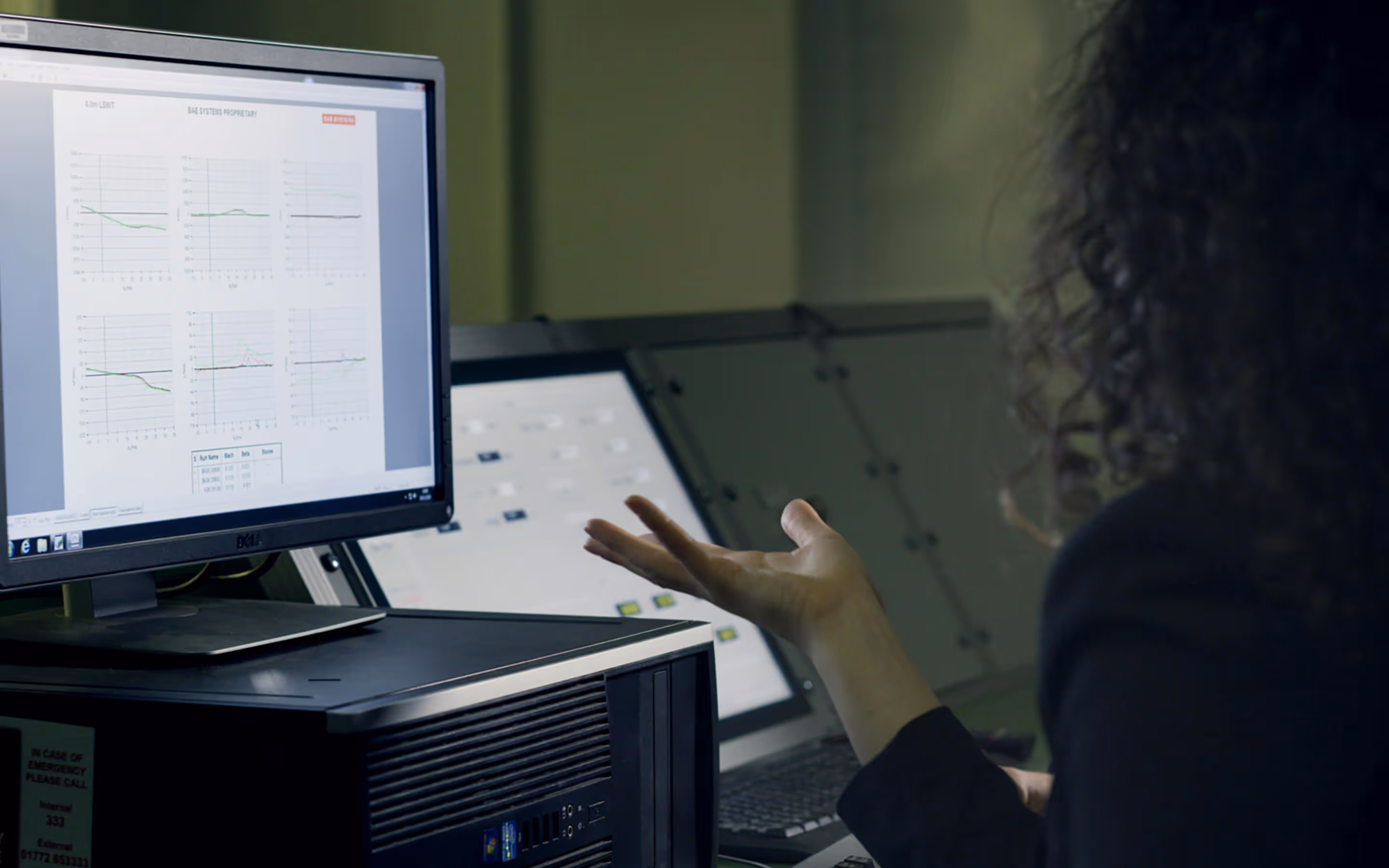 Person with curly hair gesturing towards a computer screen displaying graphs and data charts.
