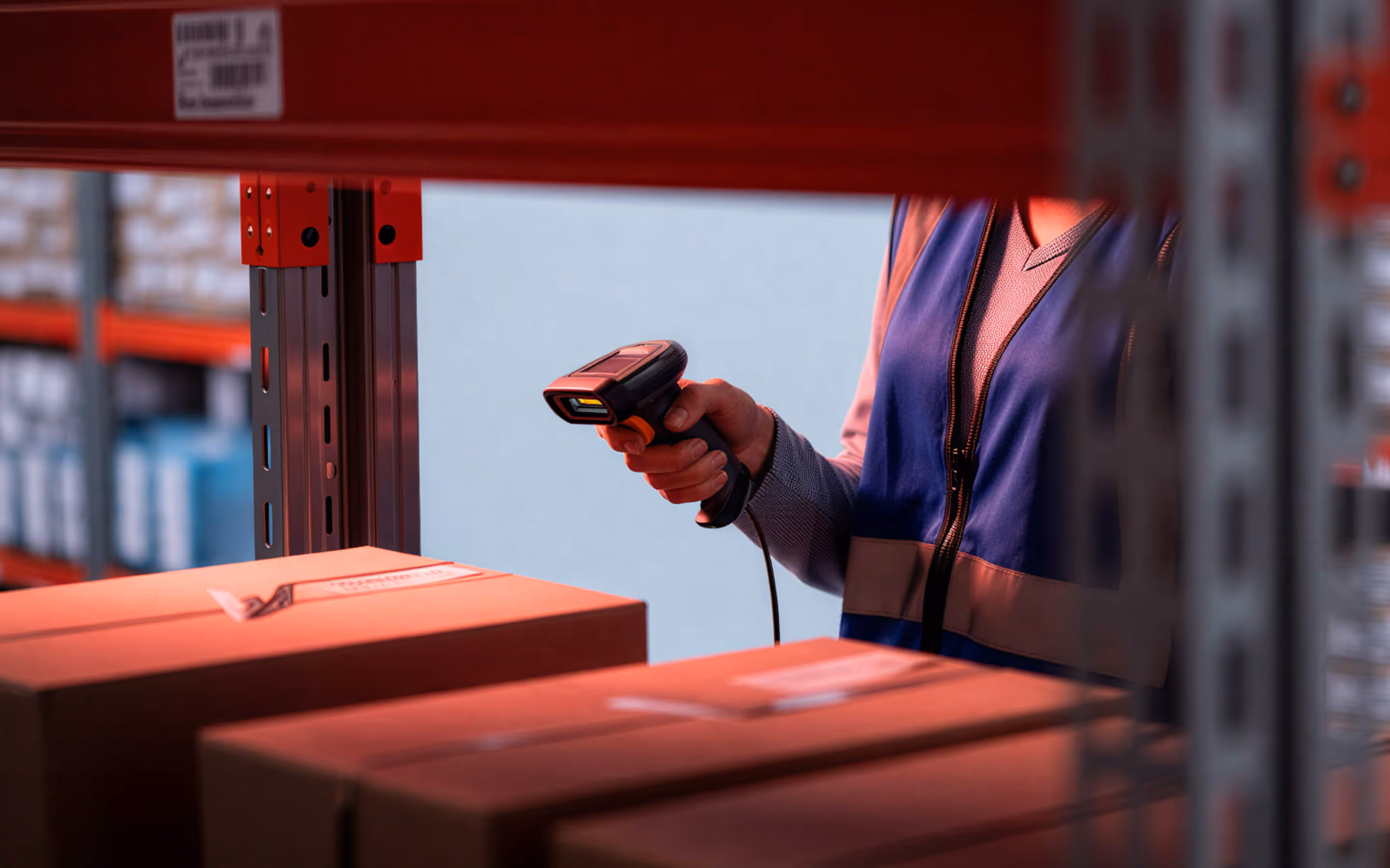 Warehouse worker scanning boxes on a shelf with a handheld barcode scanner.