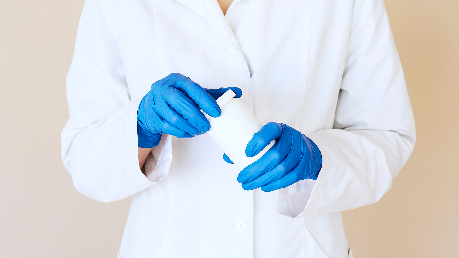 Medisch professional met blauwe handschoenen houdt een wit medicijnflesje vast.