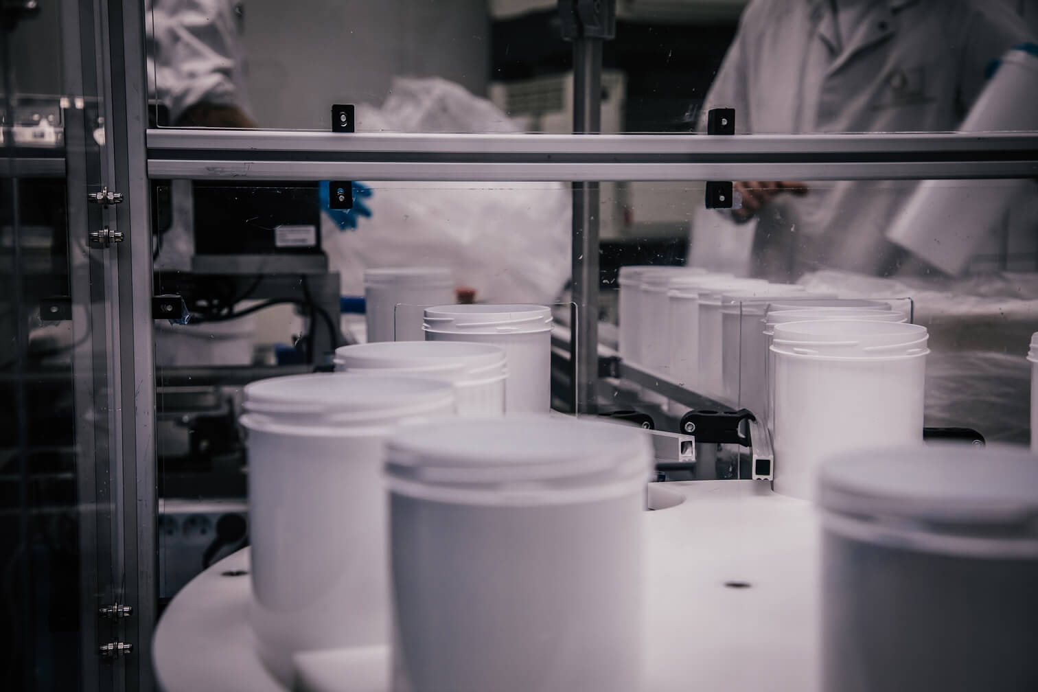 Rij witte kunststof potten op een productielijn in een schone fabriek met medewerkers in witte werkkleding.