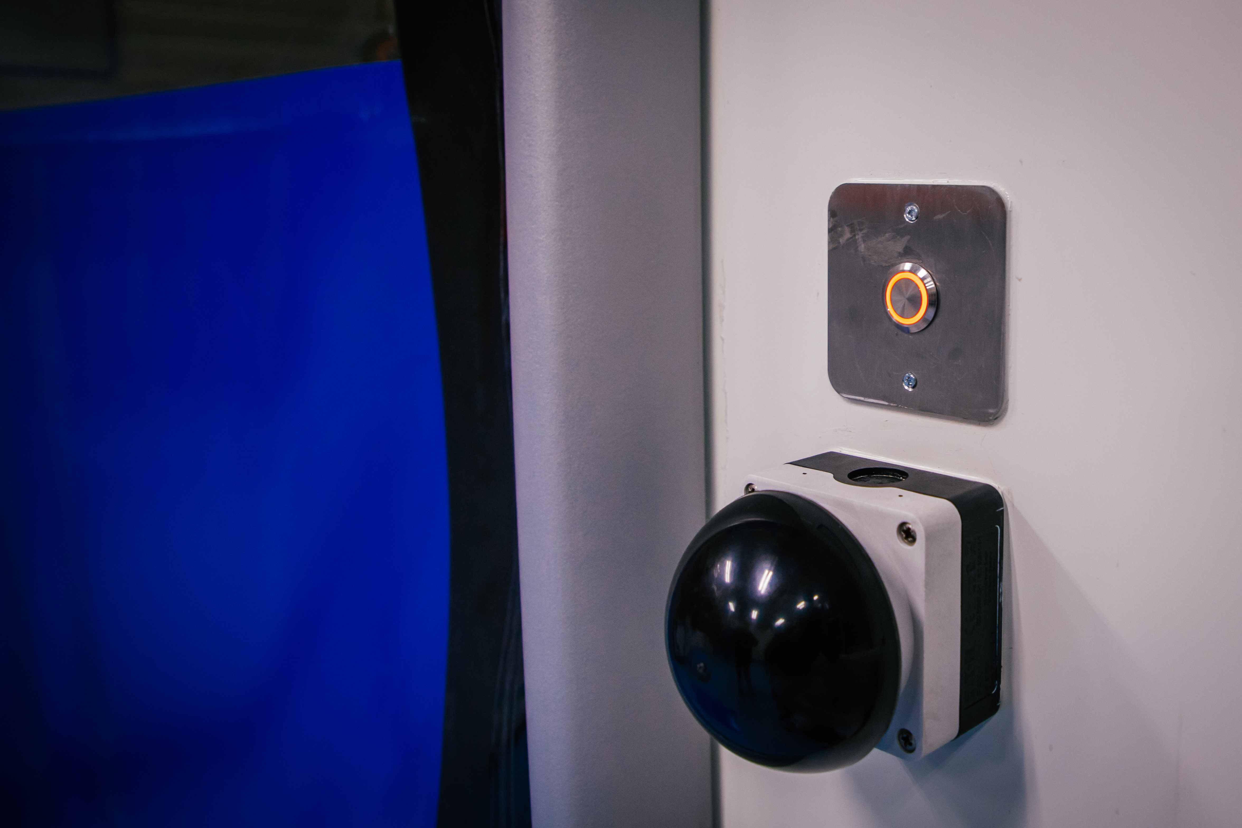 Zwarte bolvormige bediening en een verlichte oranje knop op een witte wand gemonteerd.
