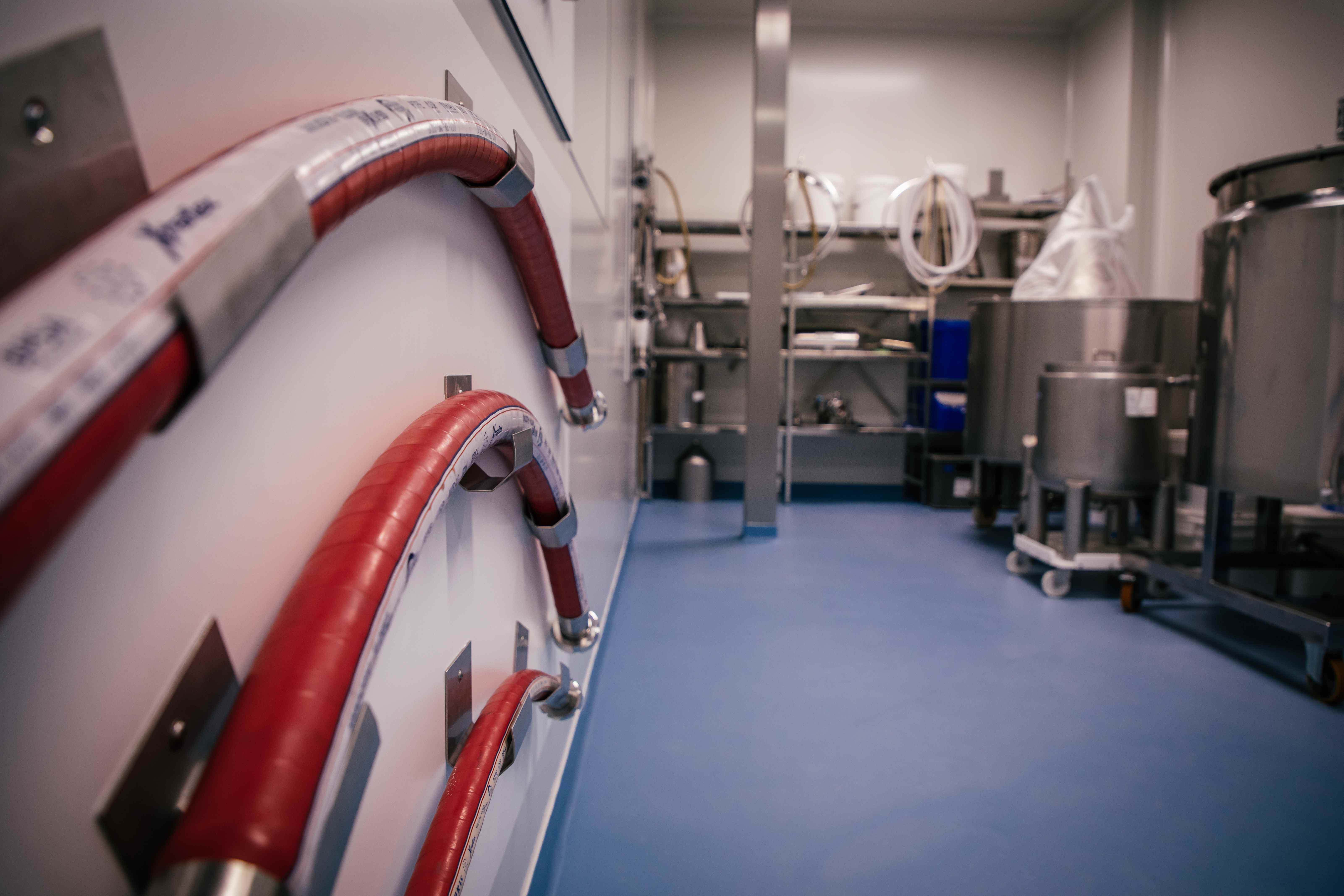 Rode ingestelde productieslangen aan een witte muur in een industriële productieruimte met roestvrijstalen apparatuur en blauwe vloer.
