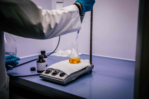 Laboratoriumtechnicus brengt vloeistof aan in een erlenmeyer-kolf met oranje vloeistof met een pipet.