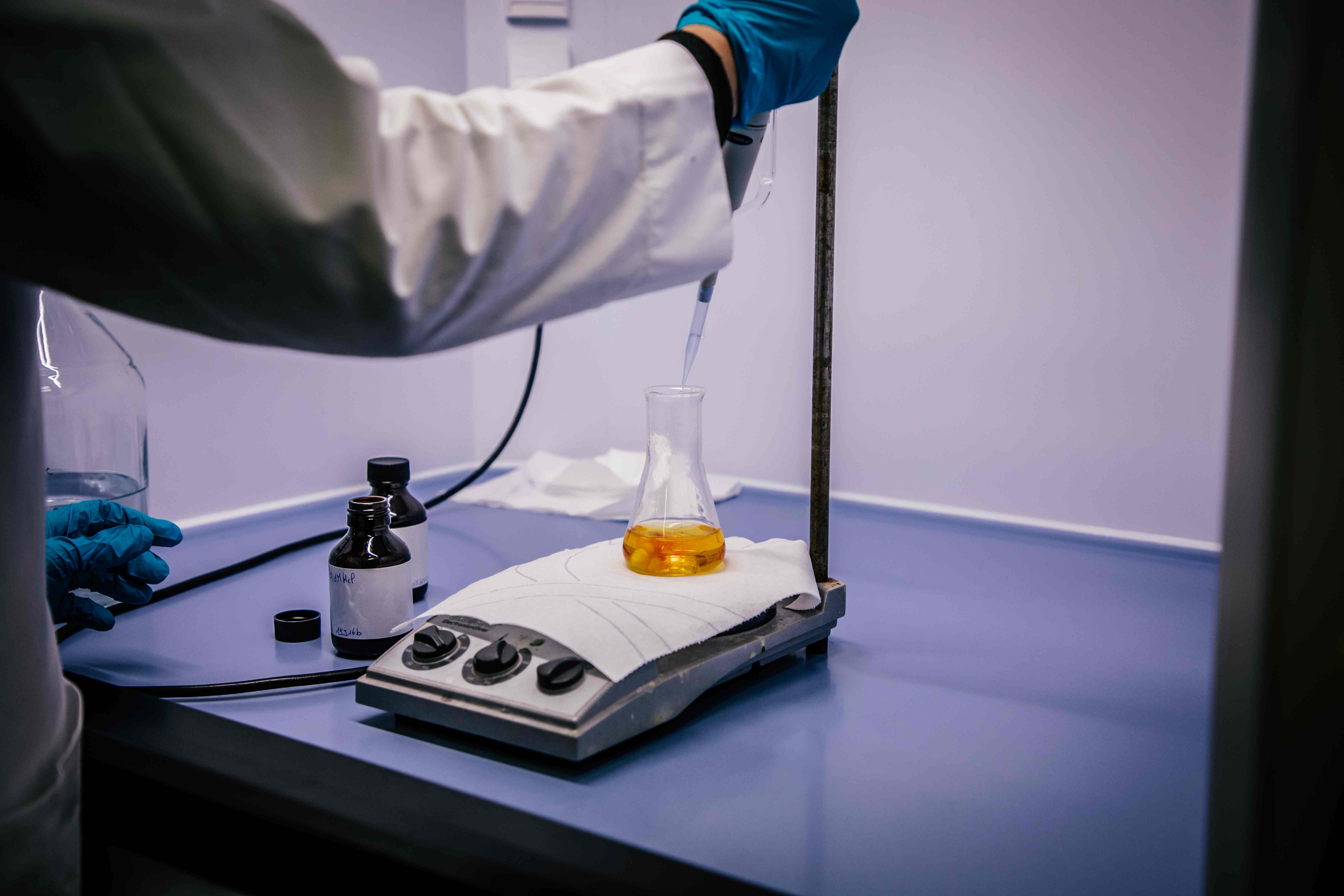 Laboratoriumtechnicus brengt vloeistof aan in een erlenmeyer-kolf met oranje vloeistof met een pipet.