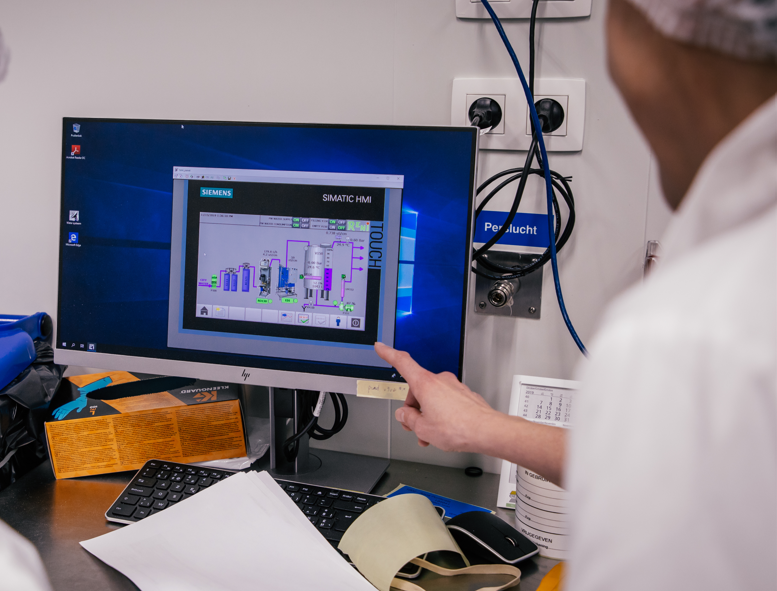 Een persoon wijst naar een computerscherm met Siemens SIMATIC HMI interface voor procesbesturing.
