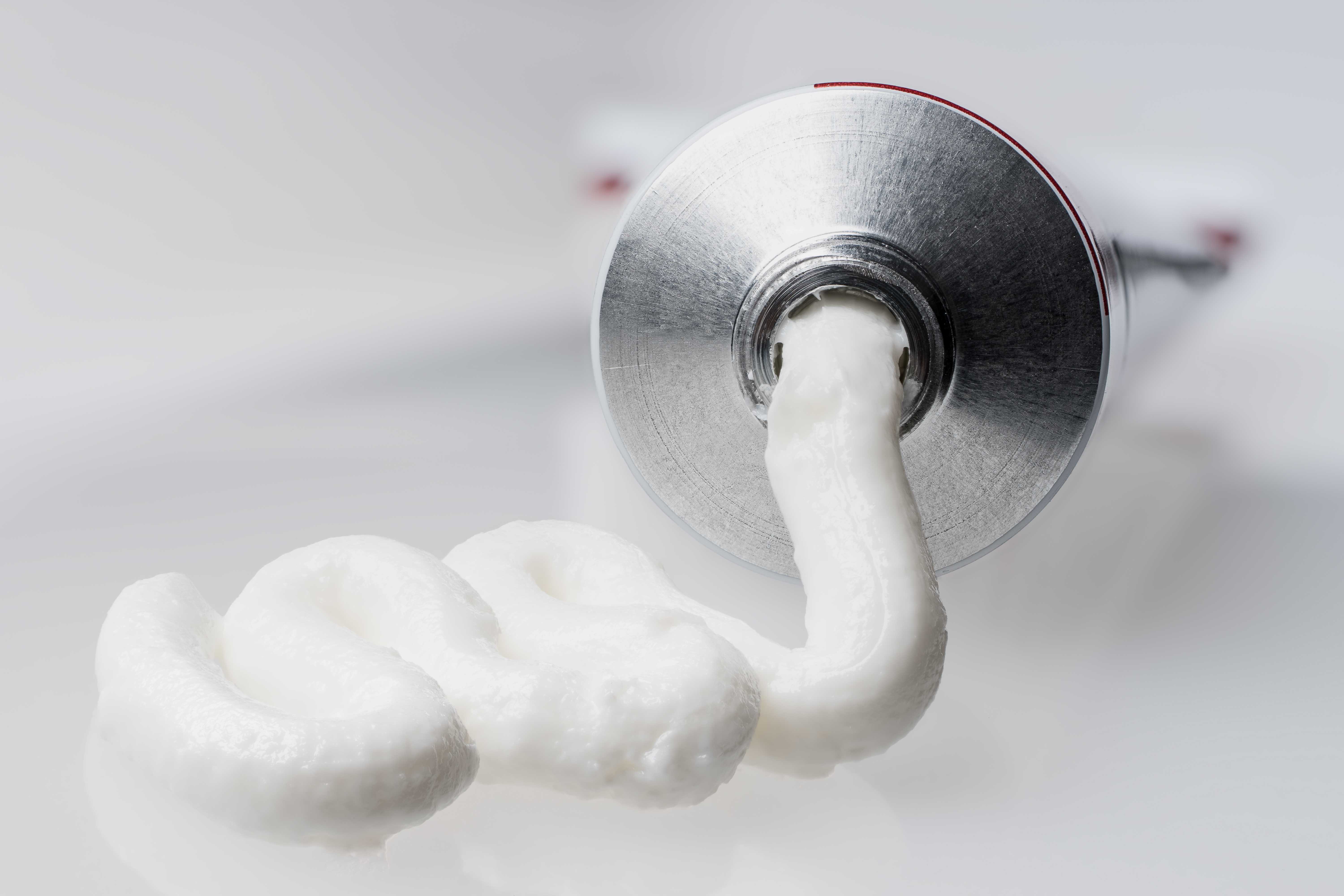 Van een metalen tube wordt een witte crèmelaag op een glad oppervlak geperst.