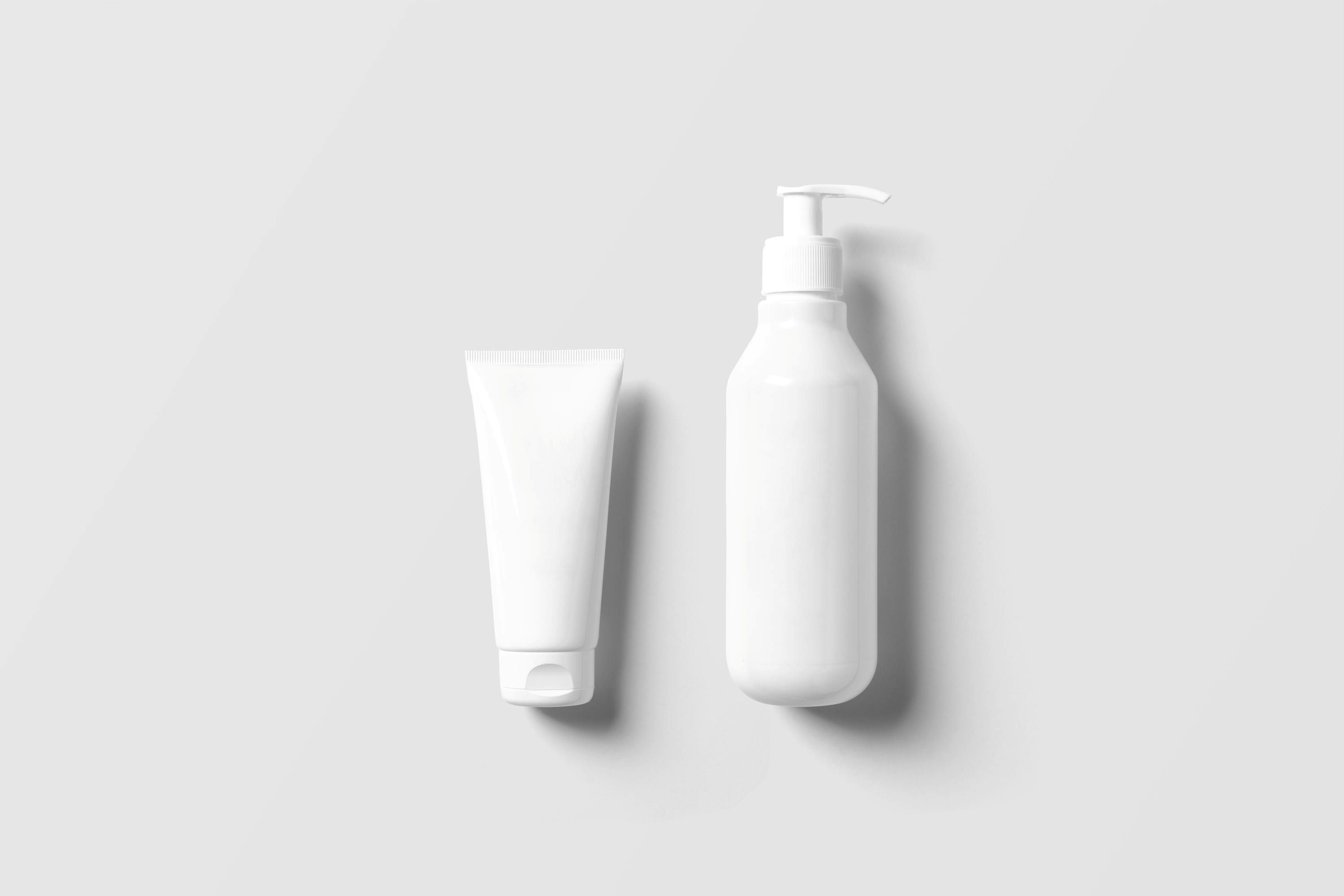 Twee lege witte cosmetische verpakkingen op een lichtgrijze achtergrond, een tube en een pompflacon.