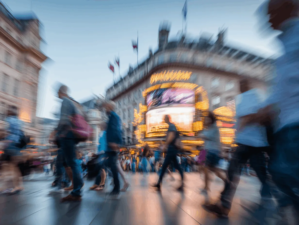 Blurred office scene with several people using laptops and tablets under warm lighting.