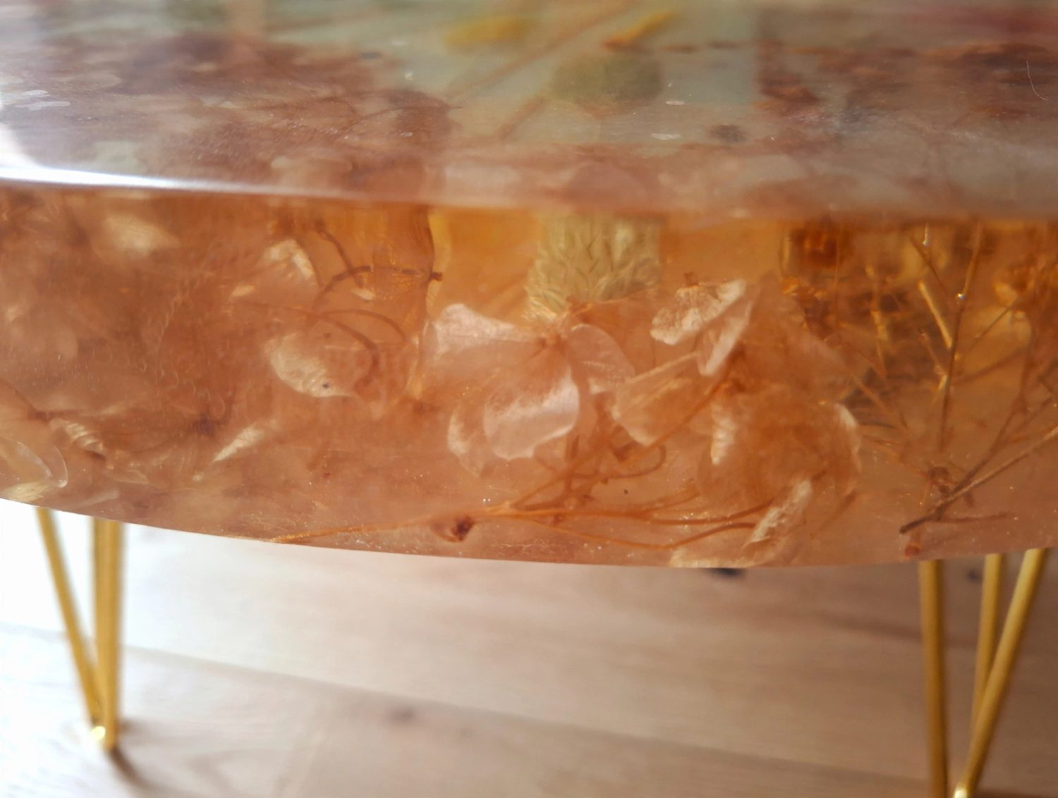 Mesa Bloom 60cm detalle resina transparente flores secas suspendida sobre parquet madera clara patas horquilla doradas 47cm altura