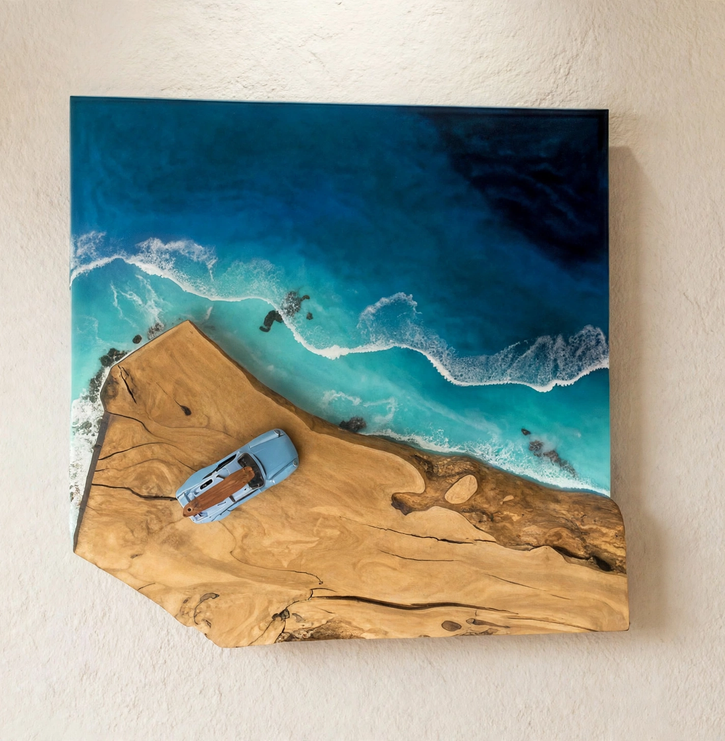 Cuadro de resina oceánica vista aérea con coche Porsche azul y tabla de surf sobre acantilado de madera de olivo y mar turquesa con olas blancas - colgado en pared blanca - hecho a mano en Mallorca por Aluna - ocean resin wall art