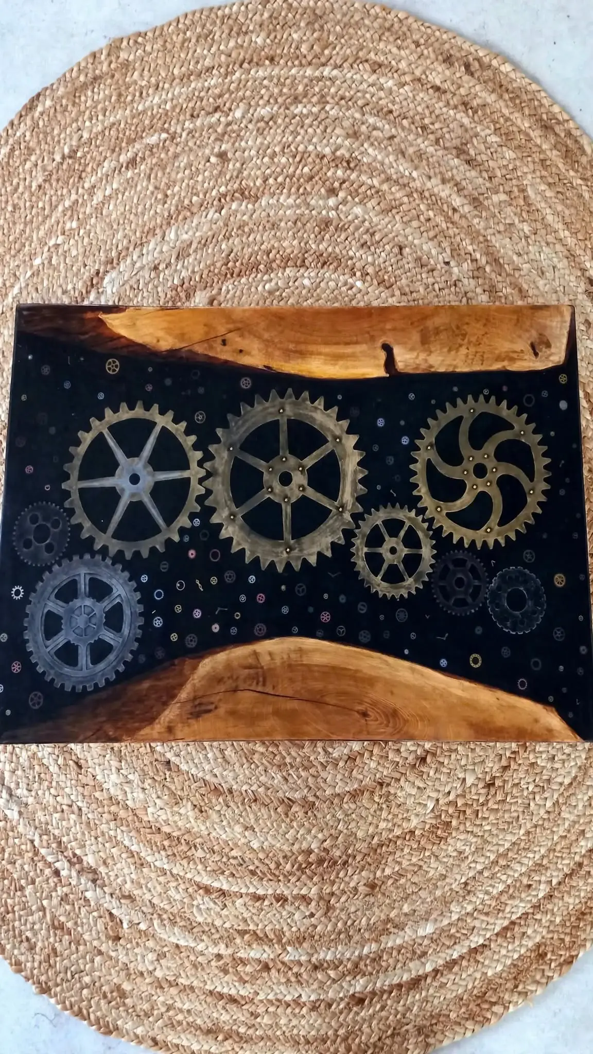Mesa baja epoxi negra con engranajes steampunk dorados y plateados sobre alfombra yute